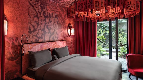 Inferno hotel room with large bed, red velvet curtains and red patterned carpet.