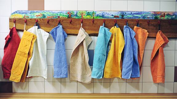 Viele kleine bunte Handtücher hängen an einem Holzbrett
