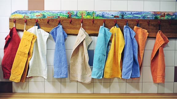 Många små färgade handdukar hänger på en träbräda med krokar