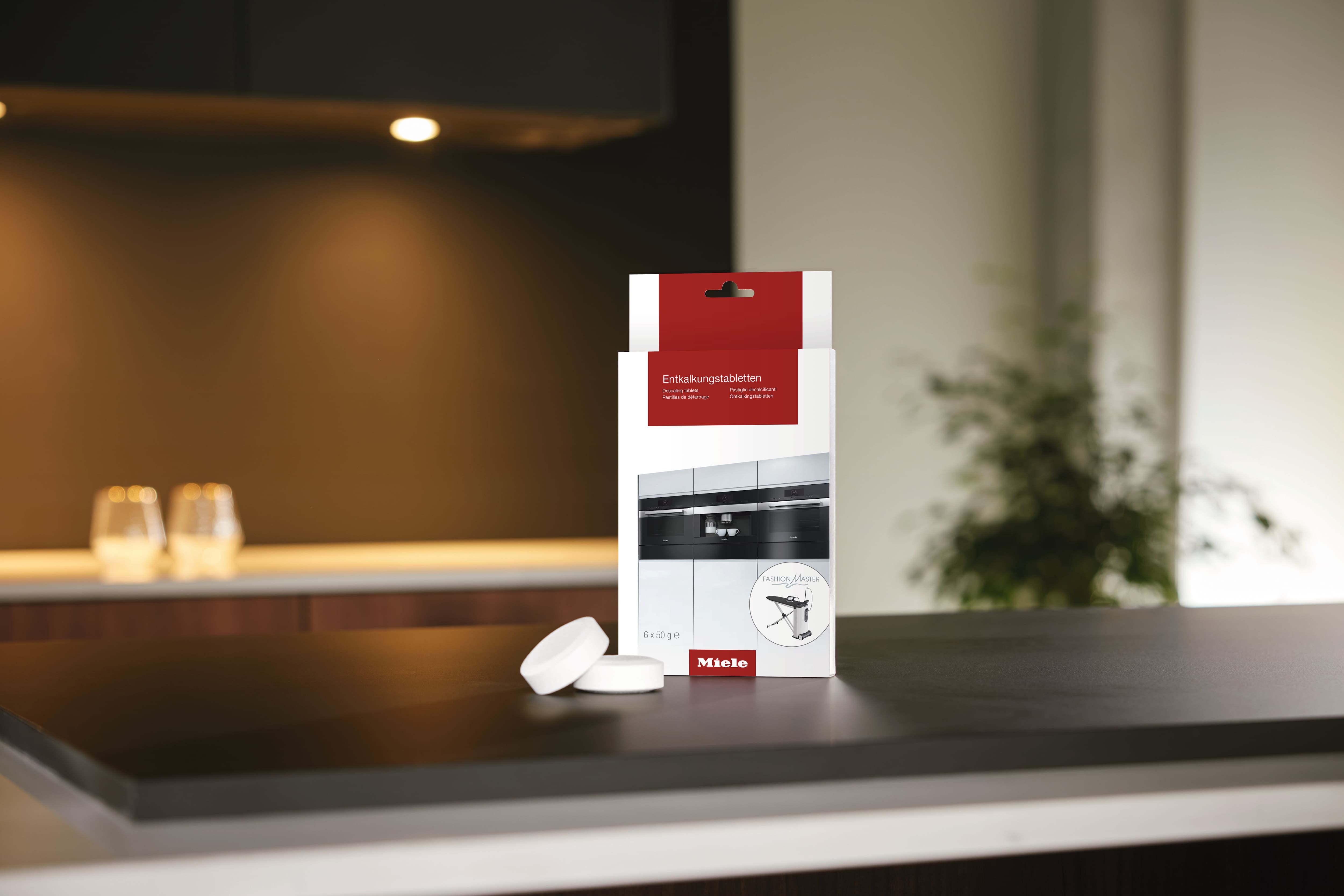 A box of Miele descaling tablets and two tablets outside the box is displayed on top of a kitchen table top