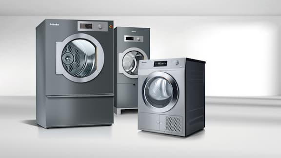 Le séchoir professionnel de référence PDR 511 gris fer se trouve à côté d'un petit séchoir géant Performance PDR 507 en acier inoxydable. Derrière les deux machines, on voit encore le séchoir SlimLine PDR 511 SL HP en gris fer.