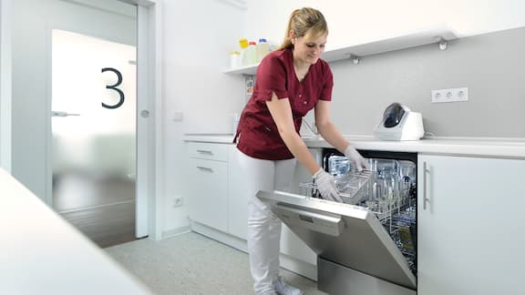 A dental assistant loads Miele Professional thermal disinfector with dentla instruments in reprocessing room