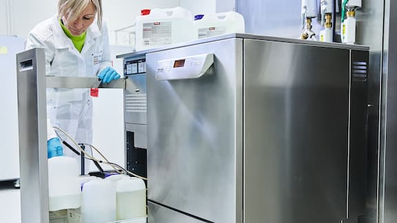 Eine Labormitarbeiterin stellt einen Reinigungsmittelkanister in eine Schublade am Laborspüler.