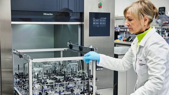 Eine Labormitarbeiterin schiebt einen mit Laborglas bestückten Korb in einen großen Laborspüler.