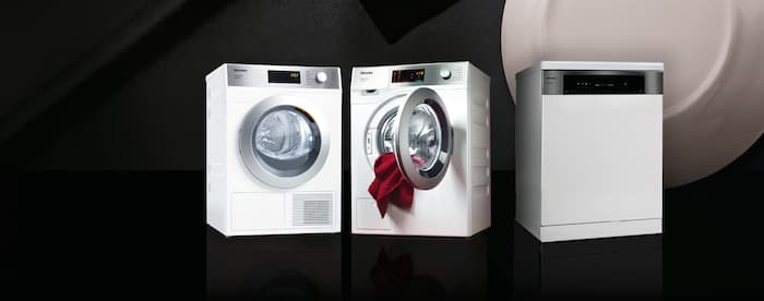 From left to right the Miele PRO Series machines MasterLine freshwater dishwasher, the steam ironing system PIB 100 and the SmartBiz washing machine are standing next to each other on a black background.