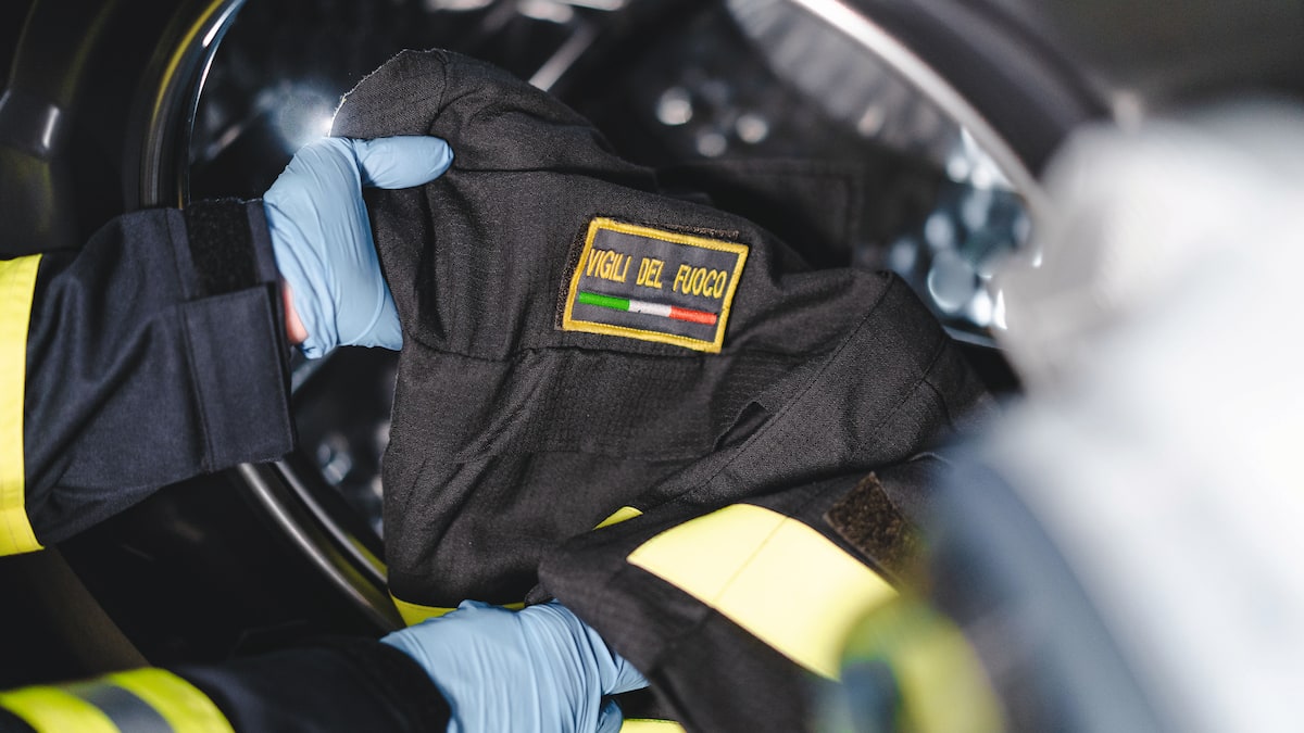 Una mano estrae un'uniforme dei vigili del fuoco da una lavatrice professionale