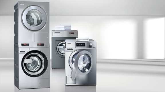 La colonne de lavage-séchage PDW 909 en acier inoxydable est placée à côté d'une petite machine à laver PWM 908 également en acier inoxydable. En arrière-plan, on peut voir une machine à laver Benchmark PWM 514 de couleur gris-fer.