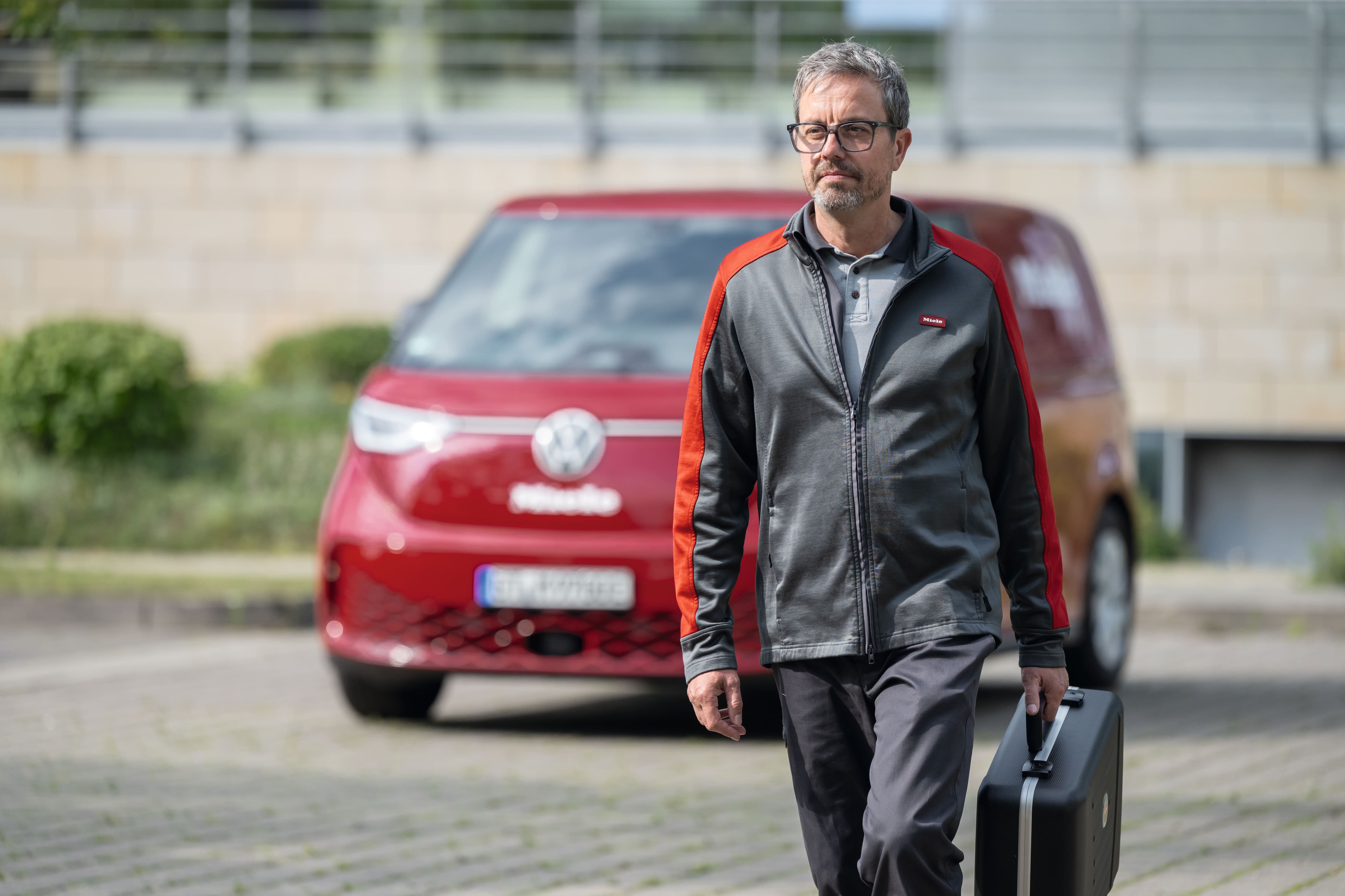 Technik Miele prochází s kufříkem nářadí kolem dodávky Miele