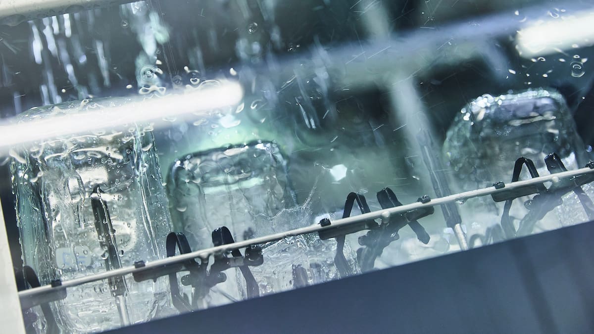Close-up of the glass door of a large-chamber laboratory washer during the cleaning process, showing water drops on the glass.