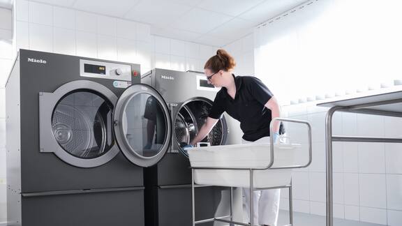 En kvinnelig ansatt legger inn i en Benchmark-vaskemaskin fra Miele Professional. 