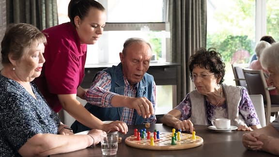 Beboere ved et bo- og omsorgssenter spiller et brettspill sammen i fellesrommet
