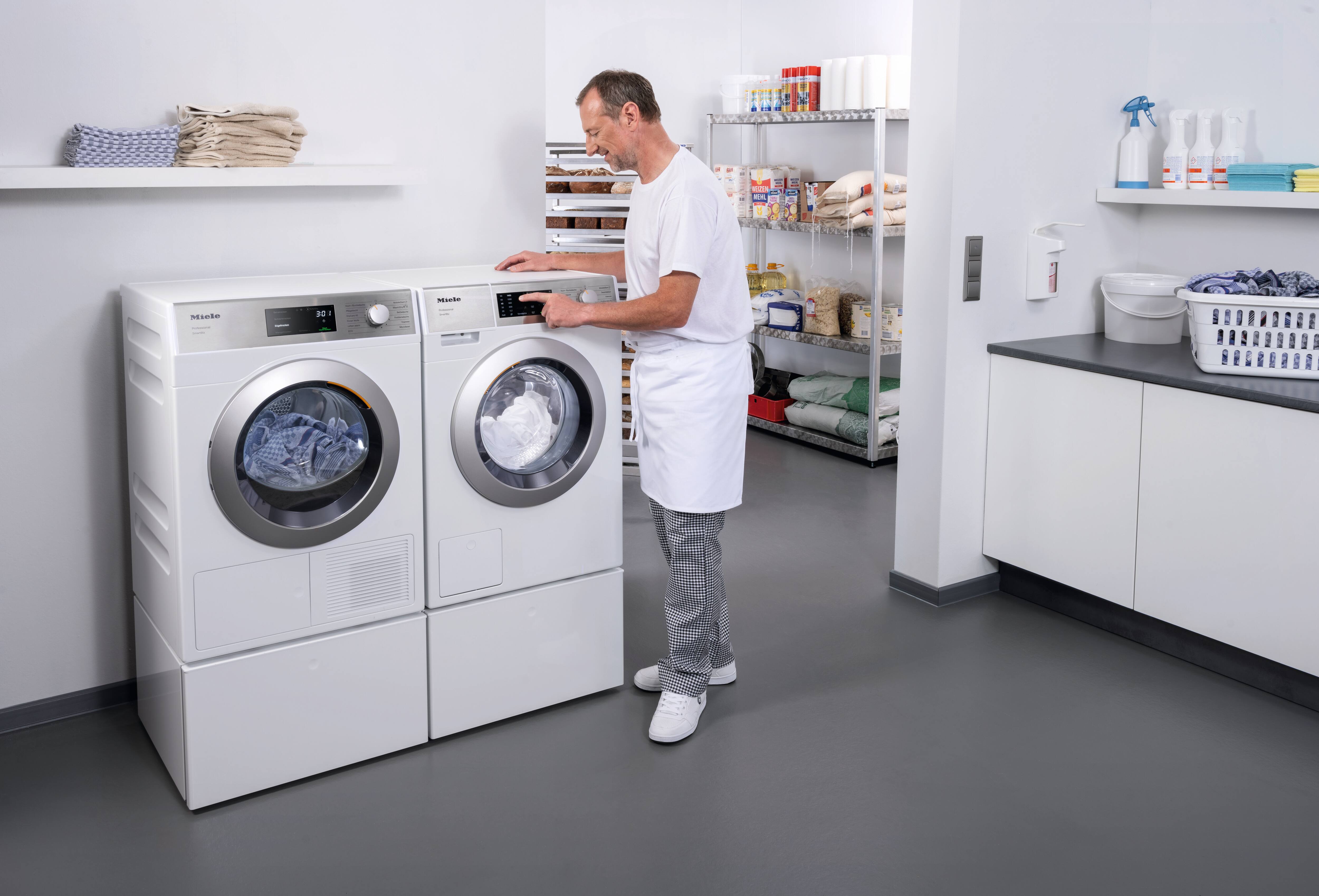 En frisør står foran Mieles SmartBiz PWM 1108-vaskemaskinen og indstiller et vaskeprogram. Ved siden af PWM 1108 står Mieles SmartBiz PDR 1108 HP-varmepumpetørretumbler