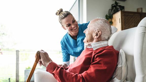 Glückliche Pflegerin kümmert sich um einen älteren Mann, der im Sessel sitzt