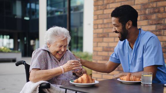 Un soignant prend le petit-déjeuner avec une résidente, en mangeant un croissant