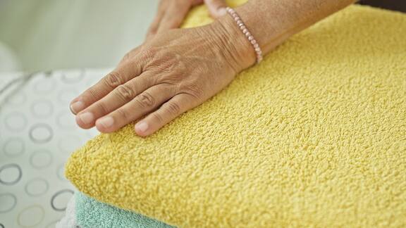 En eldre kvinne berører rene håndkler som er lagt sammen i fellesvaskeriet