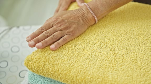 En eldre kvinne berører rene håndkler som er lagt sammen i fellesvaskeriet