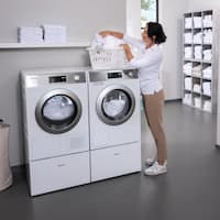 Een donkerharige vrouw staat naast een Miele SmartBiz PWM 1108 wasmachine en sorteert het wasgoed in een wasmand. Naast de wasmachine staat een Miele SmartBiz PDR 1108 HP warmtepompdroger.