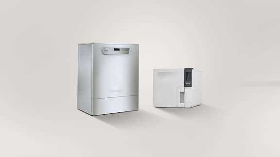 An undercounter washer-disinfector PG 85 is placed next to a Cube small steriliser on a grey background.