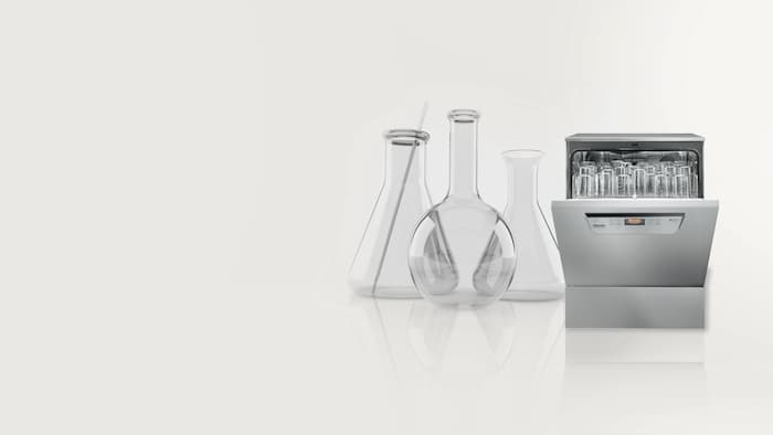 Half opened laboratory washer with laboratory glassware shown on a grey background.
