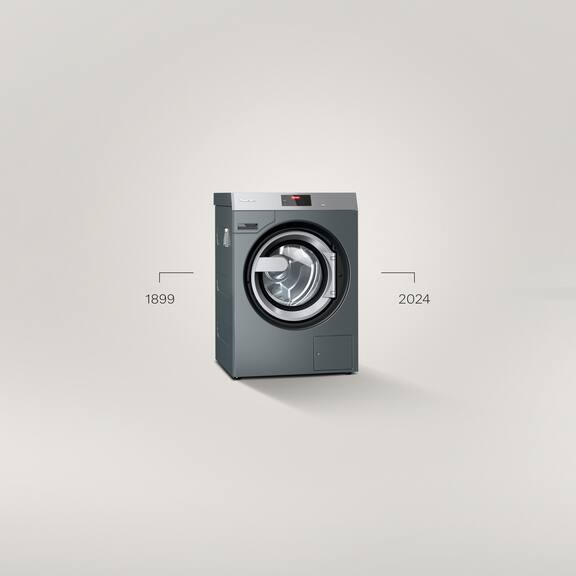 Uma máquina de lavar roupa Benchmark Performance PWM 509 encontra-se à frente de um fundo cinzento