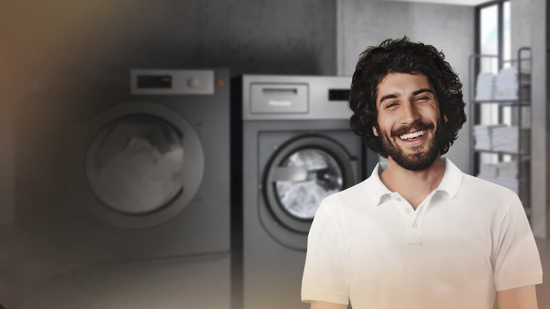 Ein Mitarbeiter im House Keeping steht lächelnd vor den Miele Benchmark Performance Waschmaschinen und Trocknern.