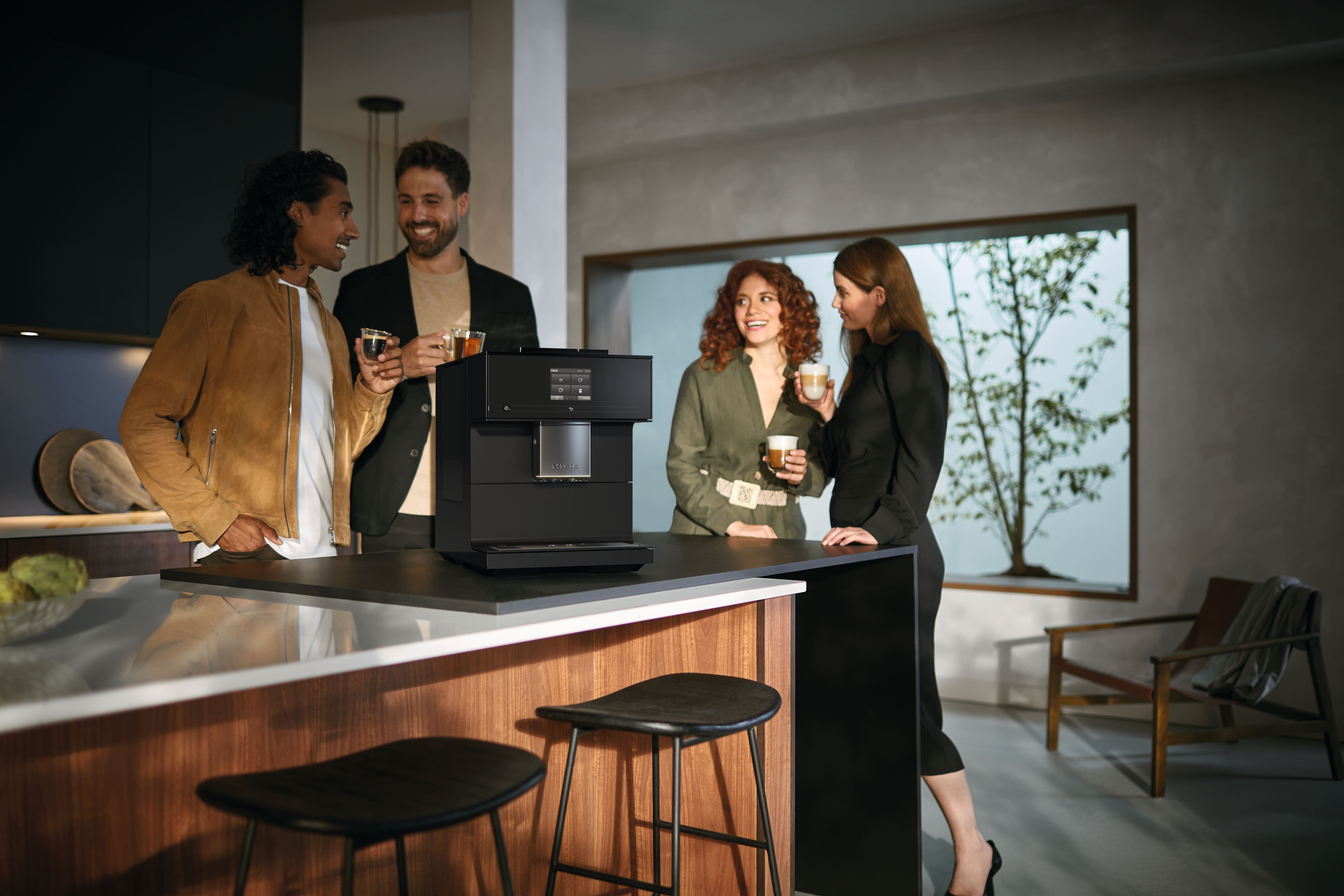 Pessoas a tomar café junto a um balcão de cozinha e máquina de café Miele