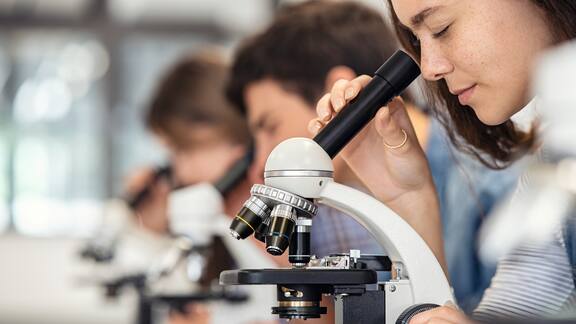 A girl sits in a classroom looking through a microscope.