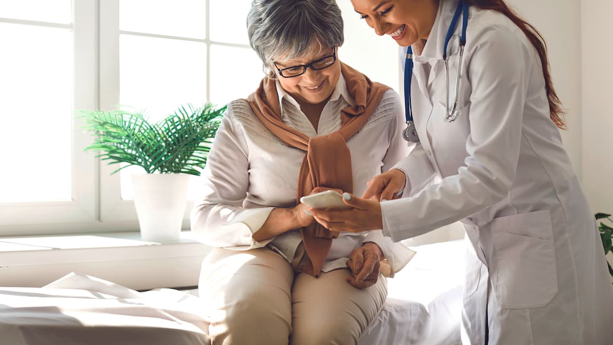 Una dottoressa è in piedi davanti a una paziente seduta e le mostra qualcosa sullo smartphone