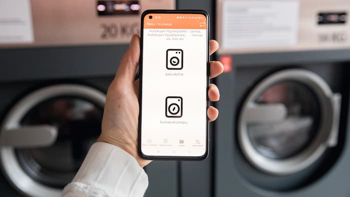 Jemand hält ein Smartphone vor eine Waschmachine, es zeigt den appWash Service.