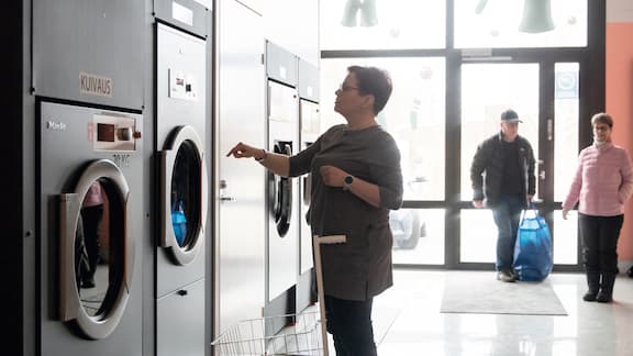 Hånd sorterer farverigt vasketøj med åben vaskemaskine i baggrunden.