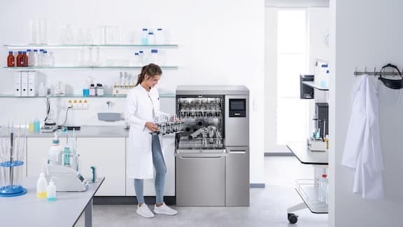 Technik laboratoryjny ładuje otwartą myjnię laboratoryjną PLW 8636, wyposażoną w moduły EasyLoad, różnymi rodzajami szkła laboratoryjnego.