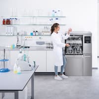 Technik laboratoryjny stoi przed otwartą myjnią laboratoryjną PLW 8636 i sprawdza czystość umytego szkła laboratoryjnego.