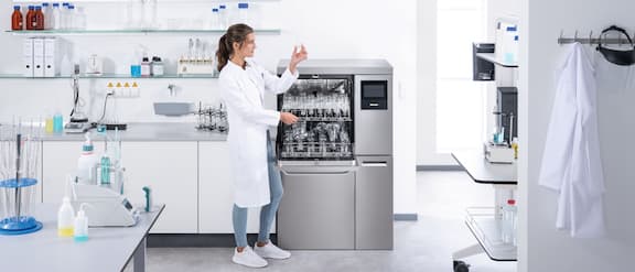 Technik laboratoryjny stoi przed otwartą myjnią laboratoryjną PLW 8636 i sprawdza czystość umytego szkła laboratoryjnego.