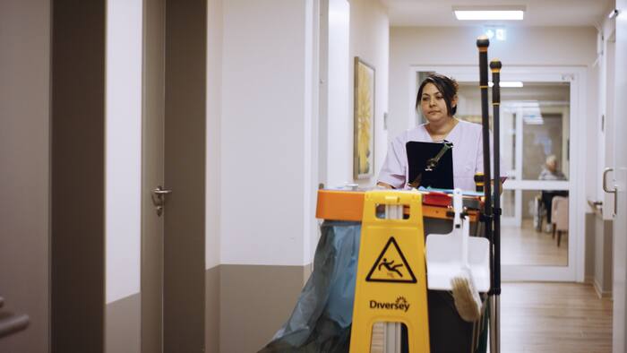 Une agente d’entretien pousse son chariot de nettoyage dans le couloir de l’établissement de soins.