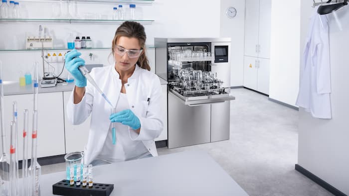 En laboratorietekniker sidder foran en halvhøj laboratorieopvaskemaskine PLW 8636 og pipetterer væske.
