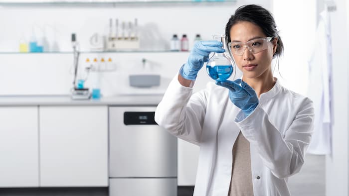 A lab technician standing in front of a run of laboratory units. The ExploreLine PLW 8604 laboratory washer in stainless steel can be seen in the background.
