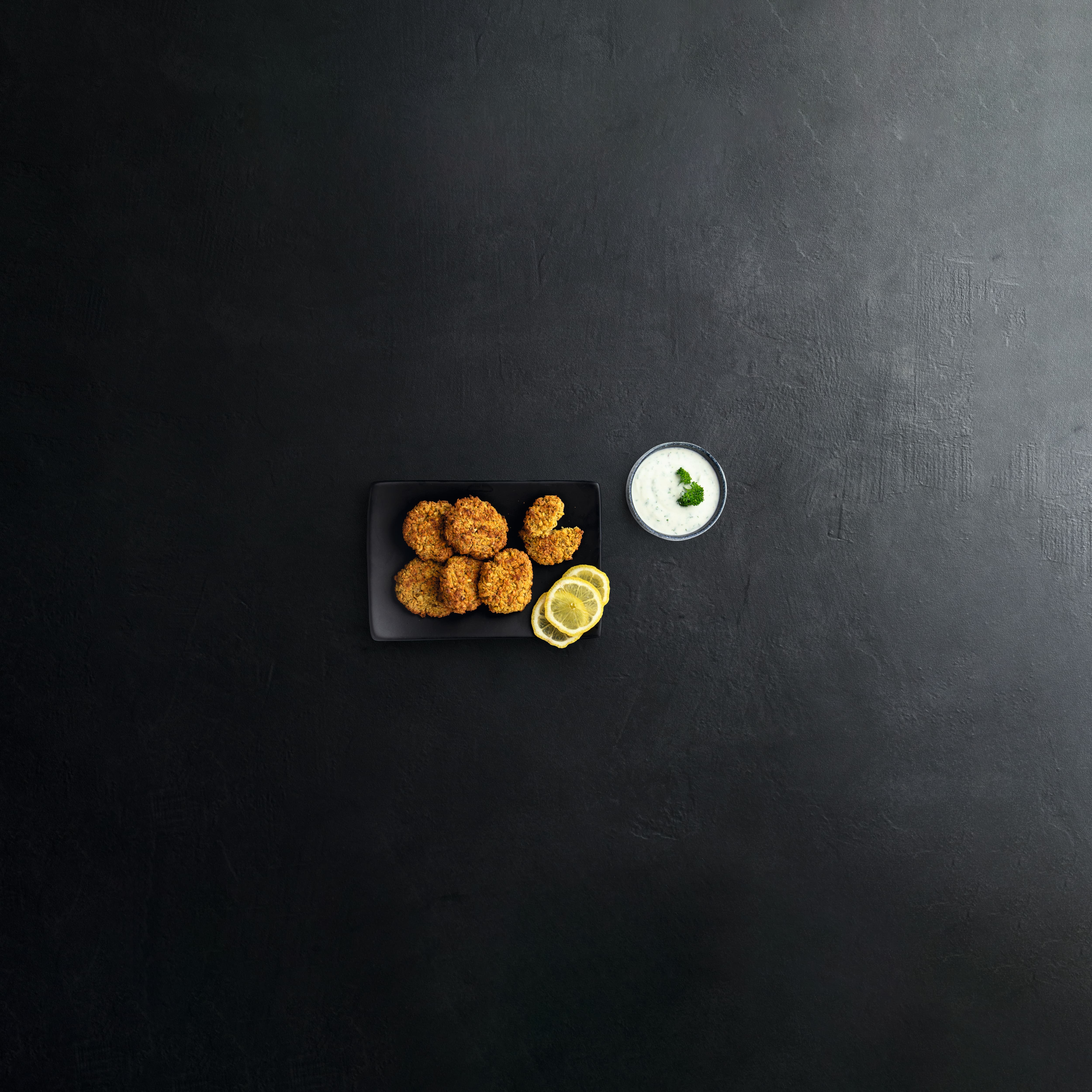 A board of fried chicken nuggets with some lemon slices on the side