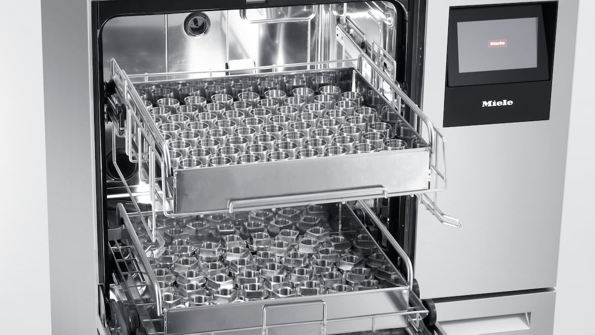 Un appareil pour le nettoyage de pièces industriel PLW 8636 présenté ouvert et équipé de diverses pièces de tournage et de fraisage utilisées dans la construction de machines.