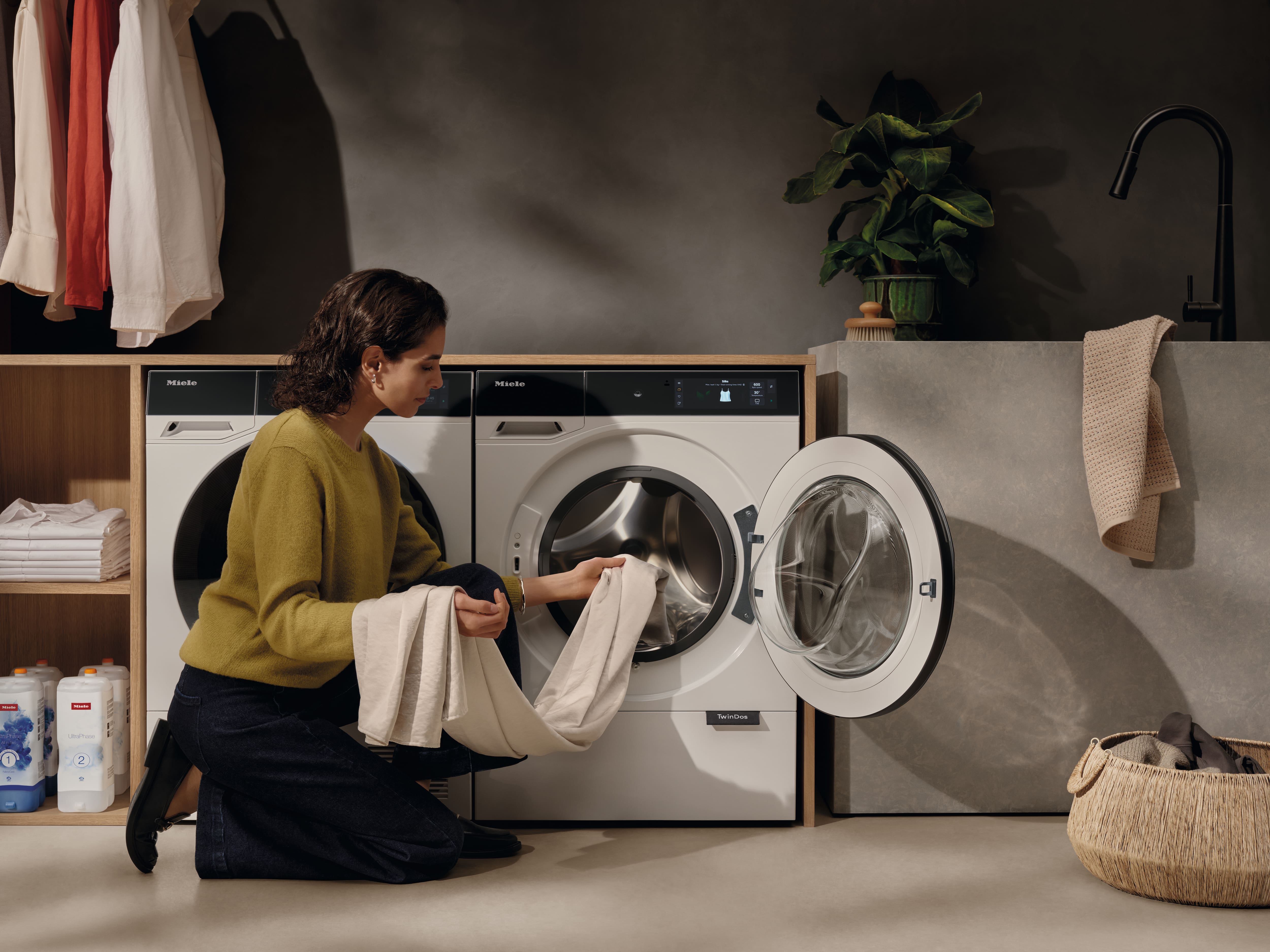 Woman in a modern laundry room unloading freshly washed clothes from a Miele Nova Series washer-dryer. Woman in a modern laundry room unloading freshly washed clothes from a Miele Nova Series washer-dryer.