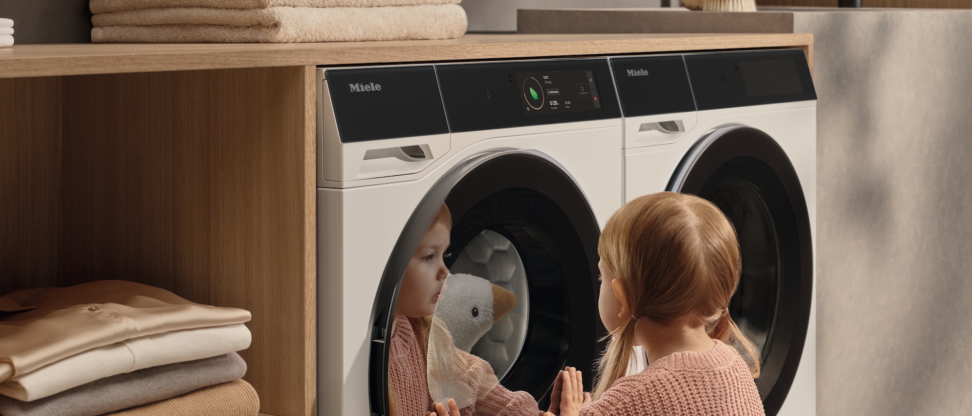Baby die kijkt in een Miele wasmachine naar haar knuffel die wordt gewassen.