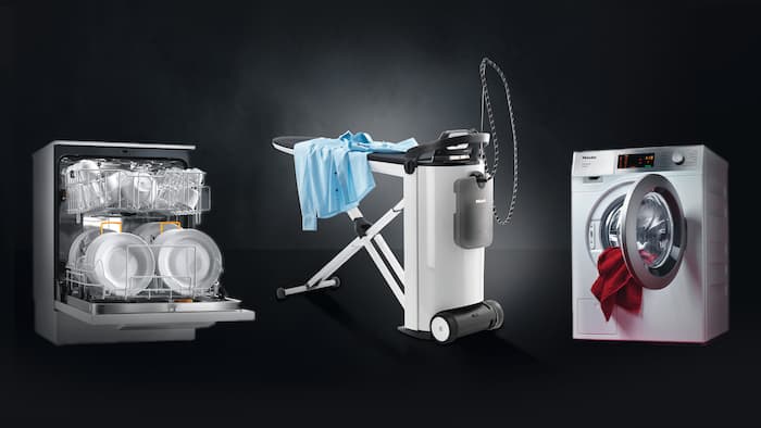 From left to right the Miele PRO Series machines MasterLine freshwater dishwasher, the steam ironing system PIB 100 and the SmartBiz washing machine are standing next to each other on a black background.