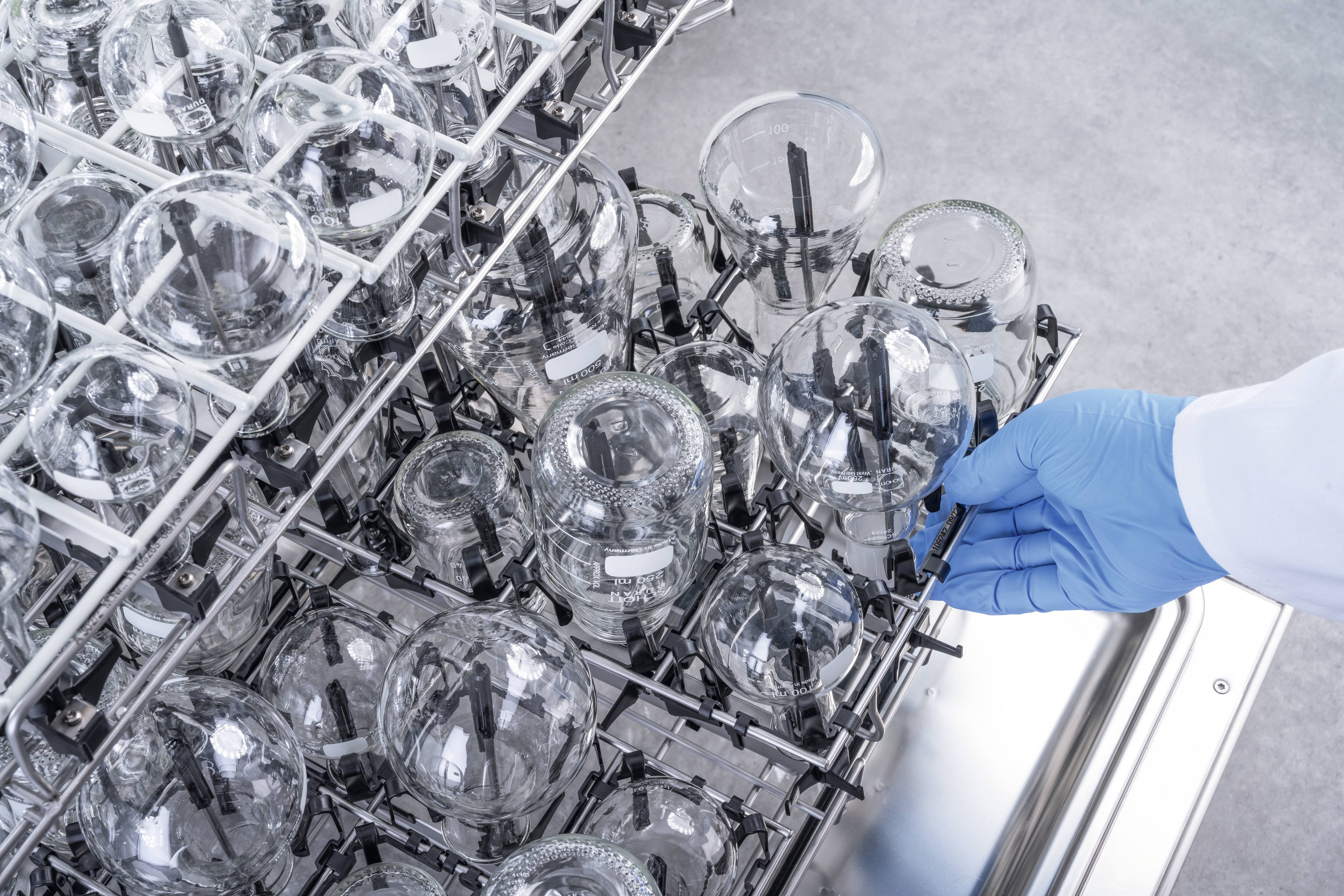 Eine Hand schiebt ein EasyLoad Modul in einen Laborspüler – bestückt mit unterschiedlichem Laborglas.