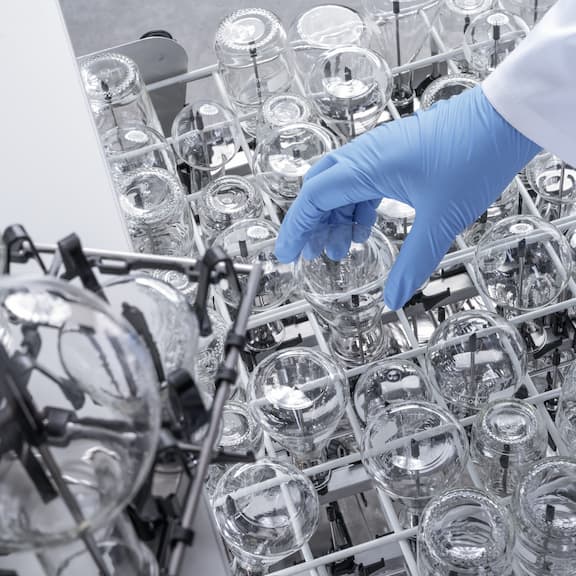 Różne moduły akcesoriów EasyLoad załadowane szkłem laboratoryjnym; ręka ładuje małe szkło laboratoryjne do modułu.