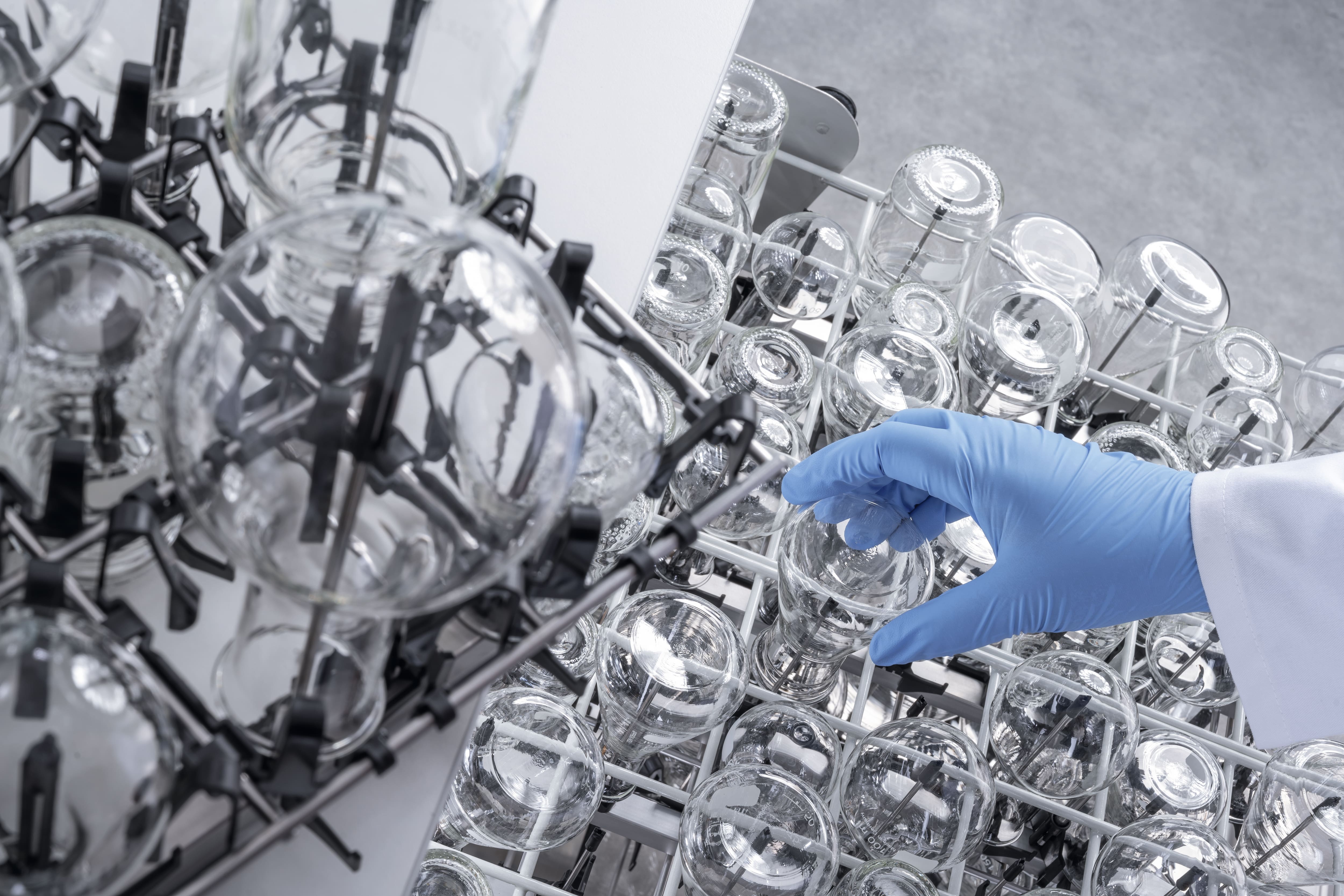 A gloved hand inserts a small Erlenmeyer flask into an EasyLoad injector module.