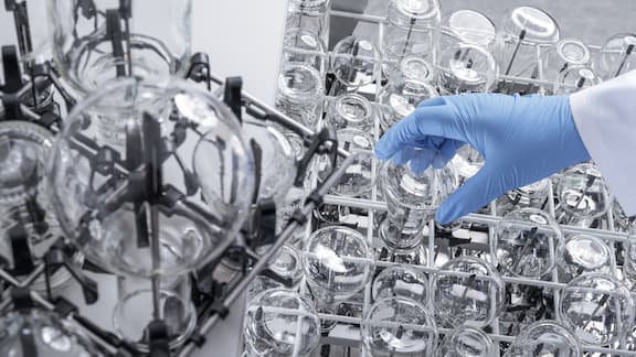 A gloved hand placing a small item of laboratory glassware in an EasyLoad insert – other laboratory glassware of various sizes has already been inserted.