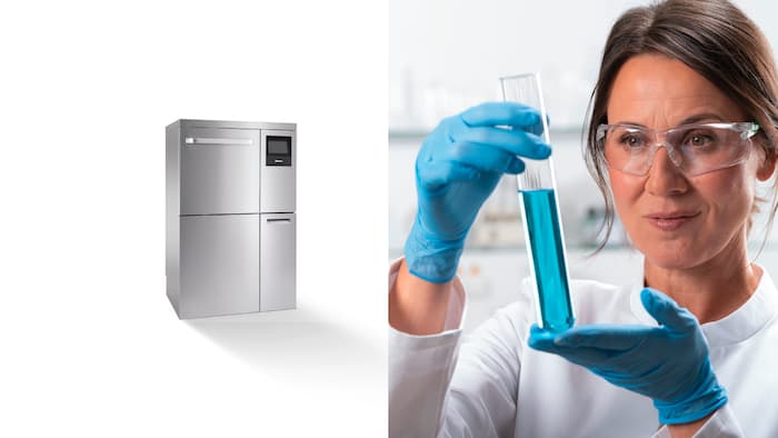 A lab technician is holding and looking at a test tube with blue liquid. To the right is a stainless steel ExpertLine PLW 8636 laboratory washer.