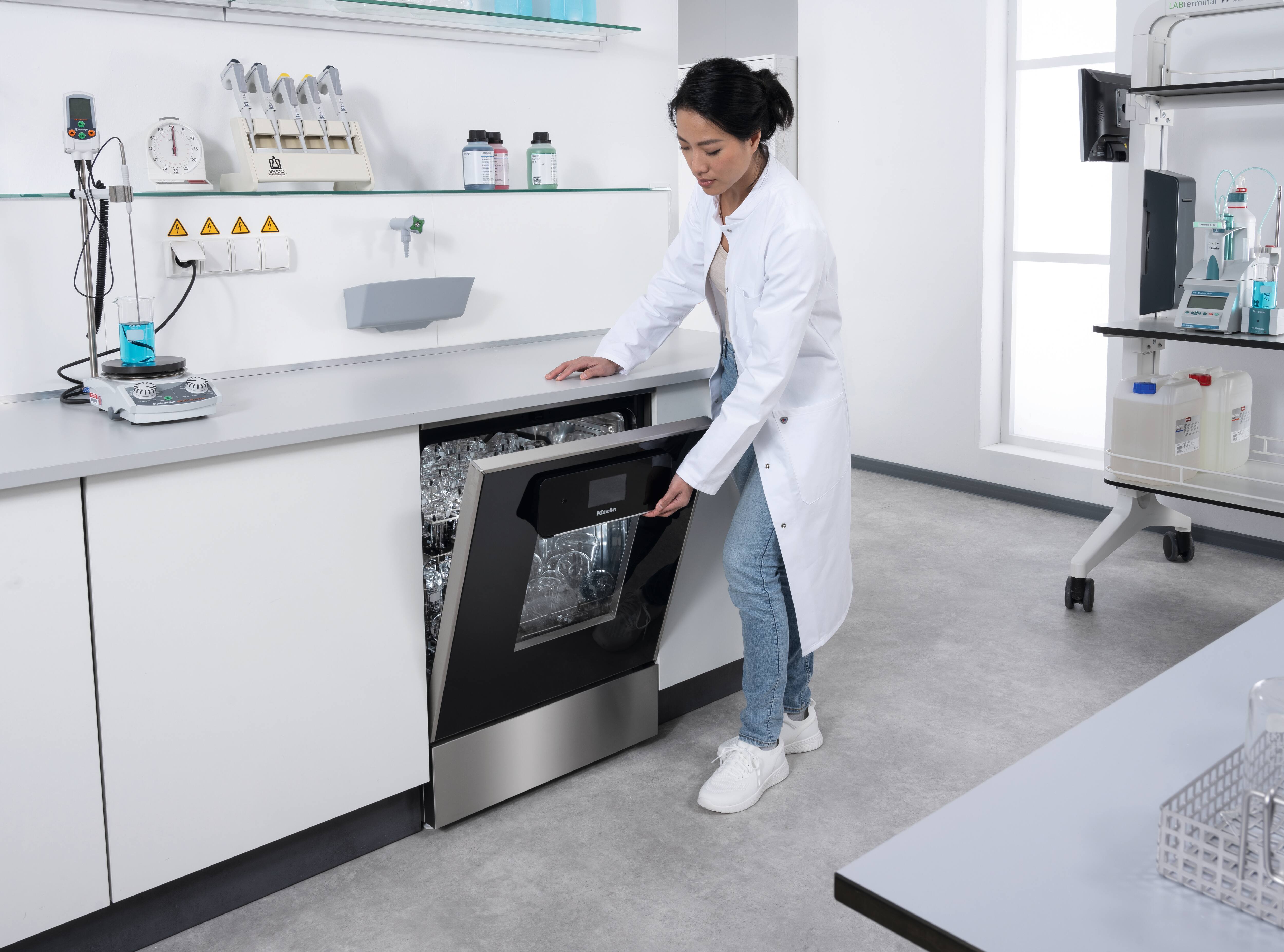 Eine Labormitarbeiterin öffnet einen Laborspüler mit einwandfrei getrocknetem Laborglas.