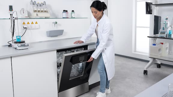 完璧に乾燥した実験用ガラス器具が入ったラボ用洗浄機を開ける検査技師。