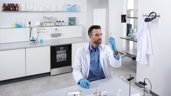 Zamestnankyňa laboratória stojí pred laboratórnou umývačkou SlimLine s Erlenmeyerovou bankou v ruke.