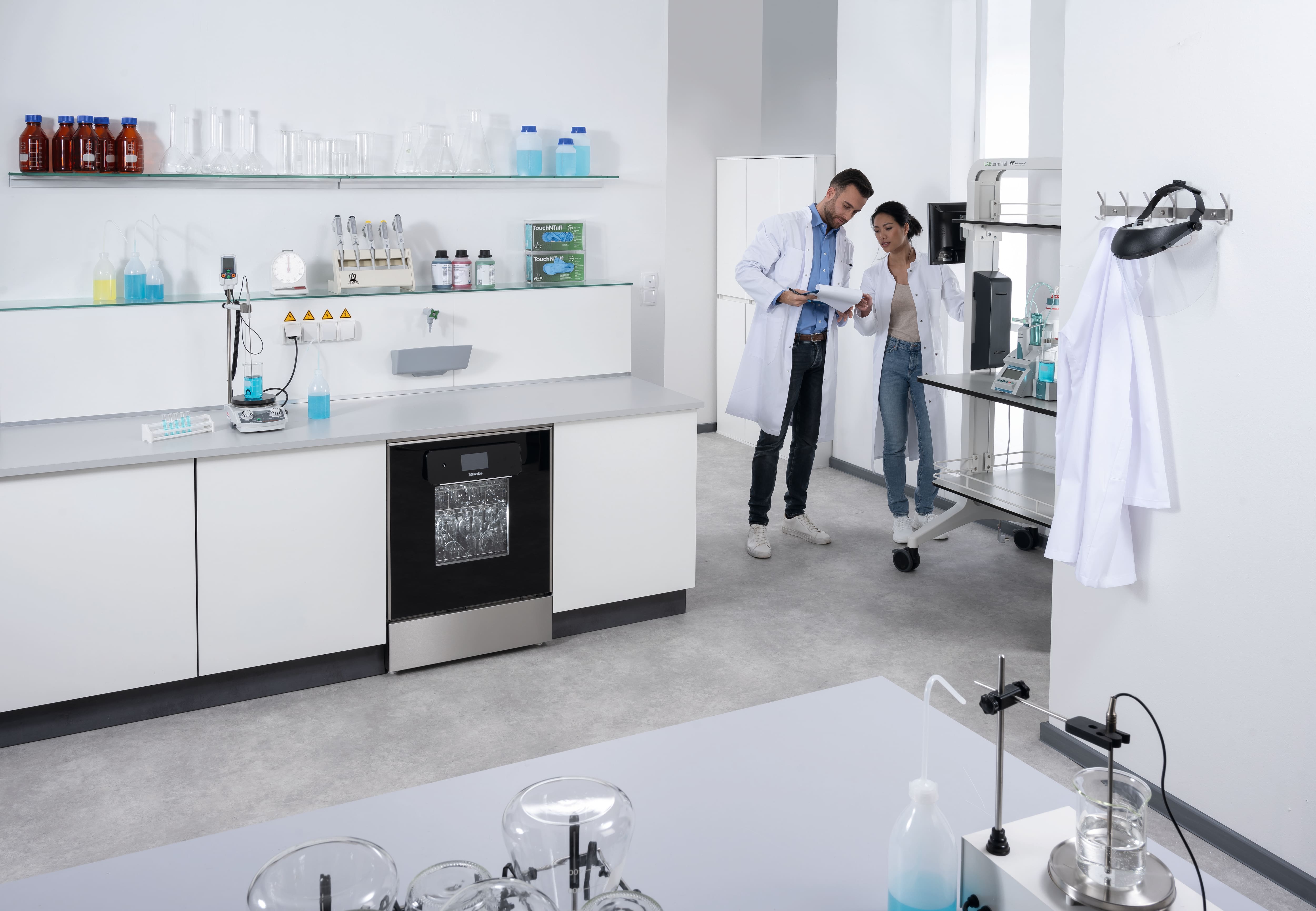 Laboratorioassistentti täyttää työtason alle asennettavan Mielen laboratoriotiskikoneen mittapullolla laboratoriohuoneessa.